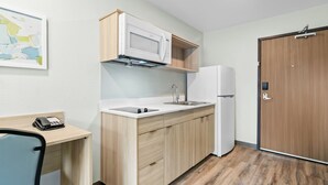 Une cuisine compacte équipée d’un four à micro-ondes, d’un réfrigérateur et d’un évier. On y trouve également un meuble en bois et un petit bureau avec une chaise.