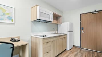 Cocina compacta con microondas, refrigerador y pileta. Hay un armario de madera y un escritorio pequeño con una silla.