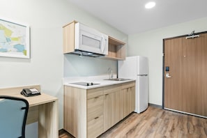 Eine kompakte Küche mit Mikrowelle, Kühlschrank und Spüle. Ein Holzkorpus und ein kleiner Schreibtisch mit Stuhl sind vorhanden.