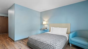 A hotel room with a bed, a nightstand, a lamp, a chair, and a wardrobe.