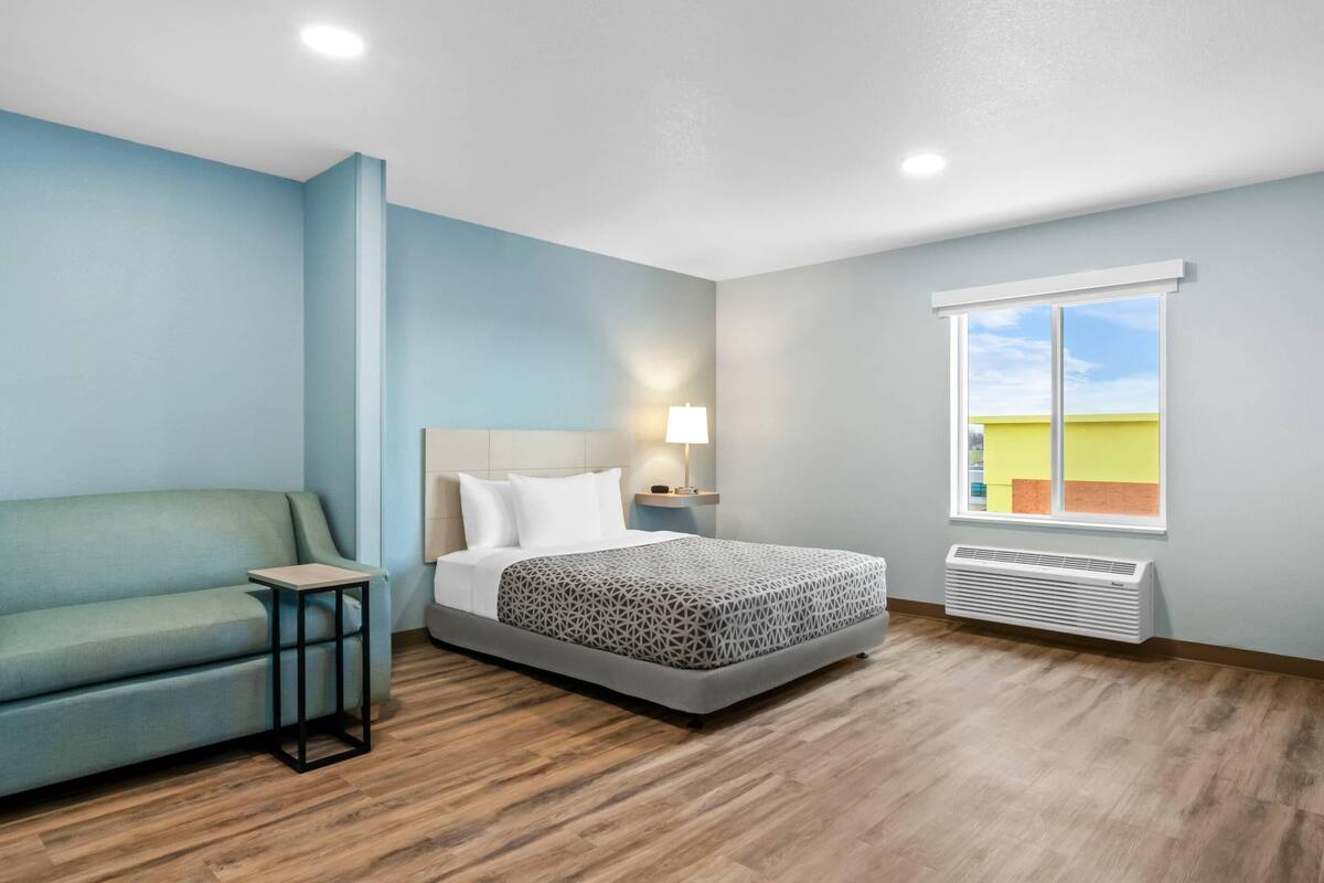 Quarto de hotel com cama, sofá, mesa de cabeceira, luminária, janela com vista e ar condicionado.