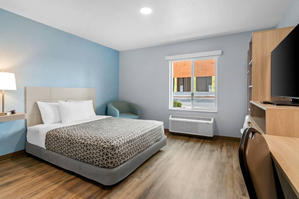 Quarto de hotel com cama, escrivaninha, televisão, janela e aquecedor fixado na parede.