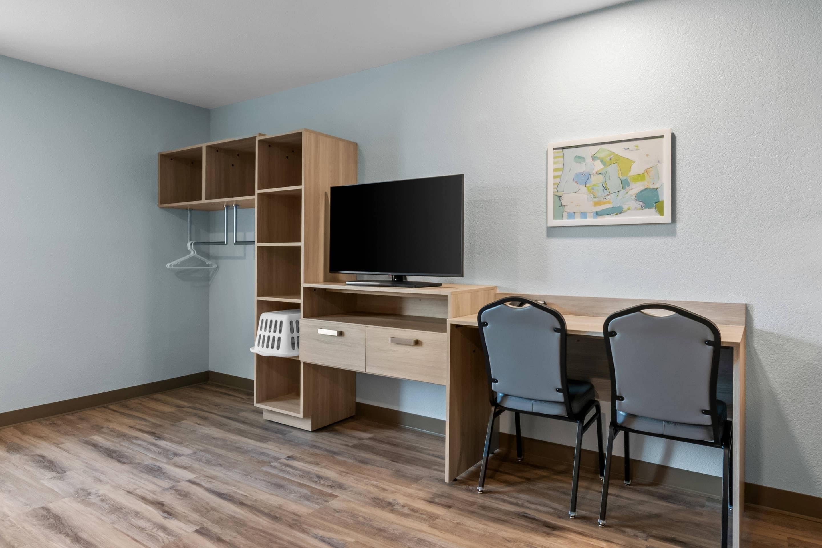 Una habitación con un escritorio de madera, dos sillas, un televisor y una obra de arte colgada en la pared.