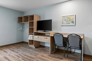 Habitació amb escriptori de fusta, dues cadires, televisió i una obra d'art penjada a la paret.