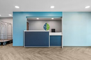 Een receptiegedeelte met een blauw-witte kleurenschema, een logo in de vorm van een blad aan de muur, en een kar met metalen palen.