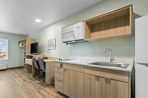 A modern kitchen with wooden cabinets, a built-in microwave, a sink, and a television. - Woodspring Suites Rogers Bentonville (Lowell)