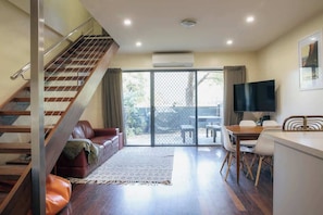 A spacious living area with a staircase, a sofa, a TV, and a dining table.