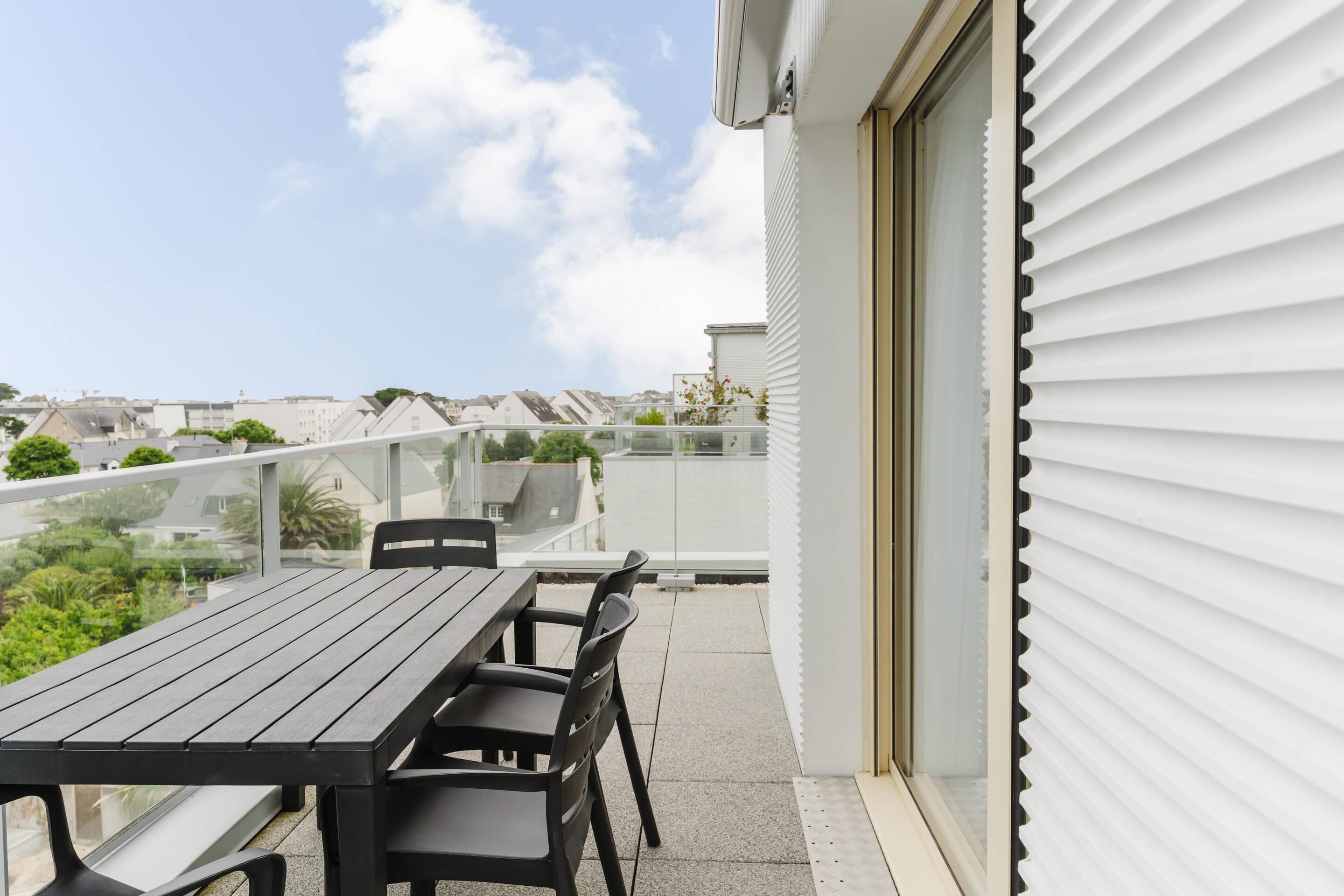 Ein Balkon mit Tisch und Stühlen, Geländer aus Glas und Blick auf die Stadtlandschaft.