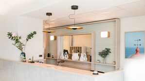 Un espace d’accueil doté d’un comptoir en marbre, de luminaires suspendus, d’un grand miroir et offrant une vue sur la mer par une fenêtre.