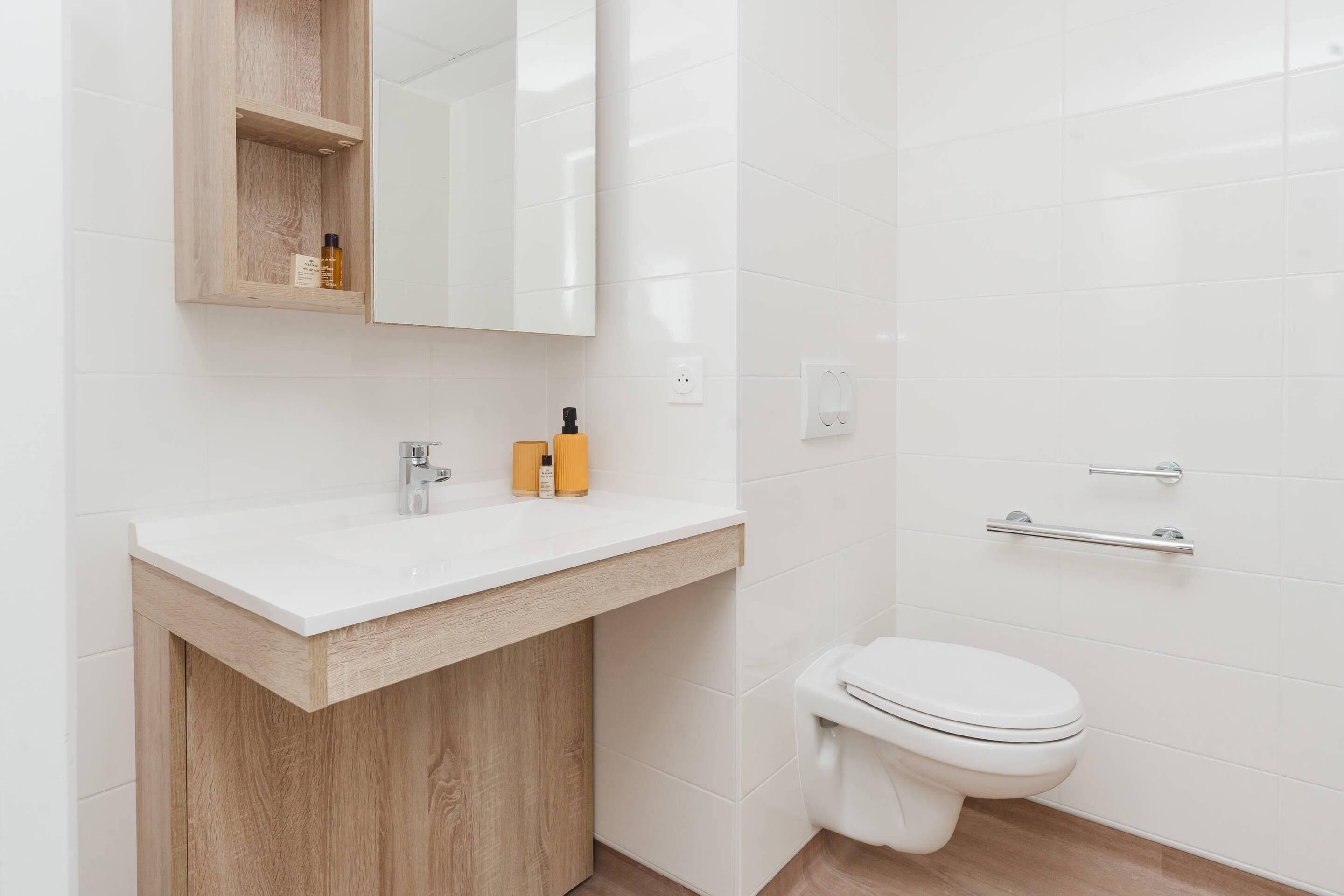 A modern bathroom with a white sink, wooden vanity, and a white toilet.