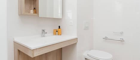 A modern bathroom with a white sink, wooden vanity, and a white toilet.