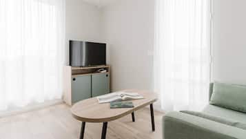 Una sala de estar moderna con un televisor de pantalla plana sobre un soporte de madera, un sofá de color claro y una mesita con un libro.
