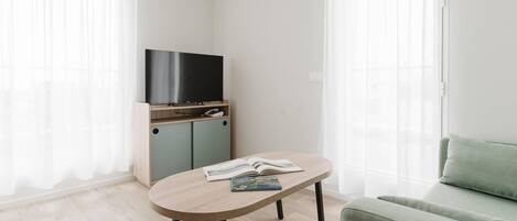 Una sala de estar moderna con un televisor de pantalla plana sobre un soporte de madera, un sofá de color claro y una mesita con un libro.