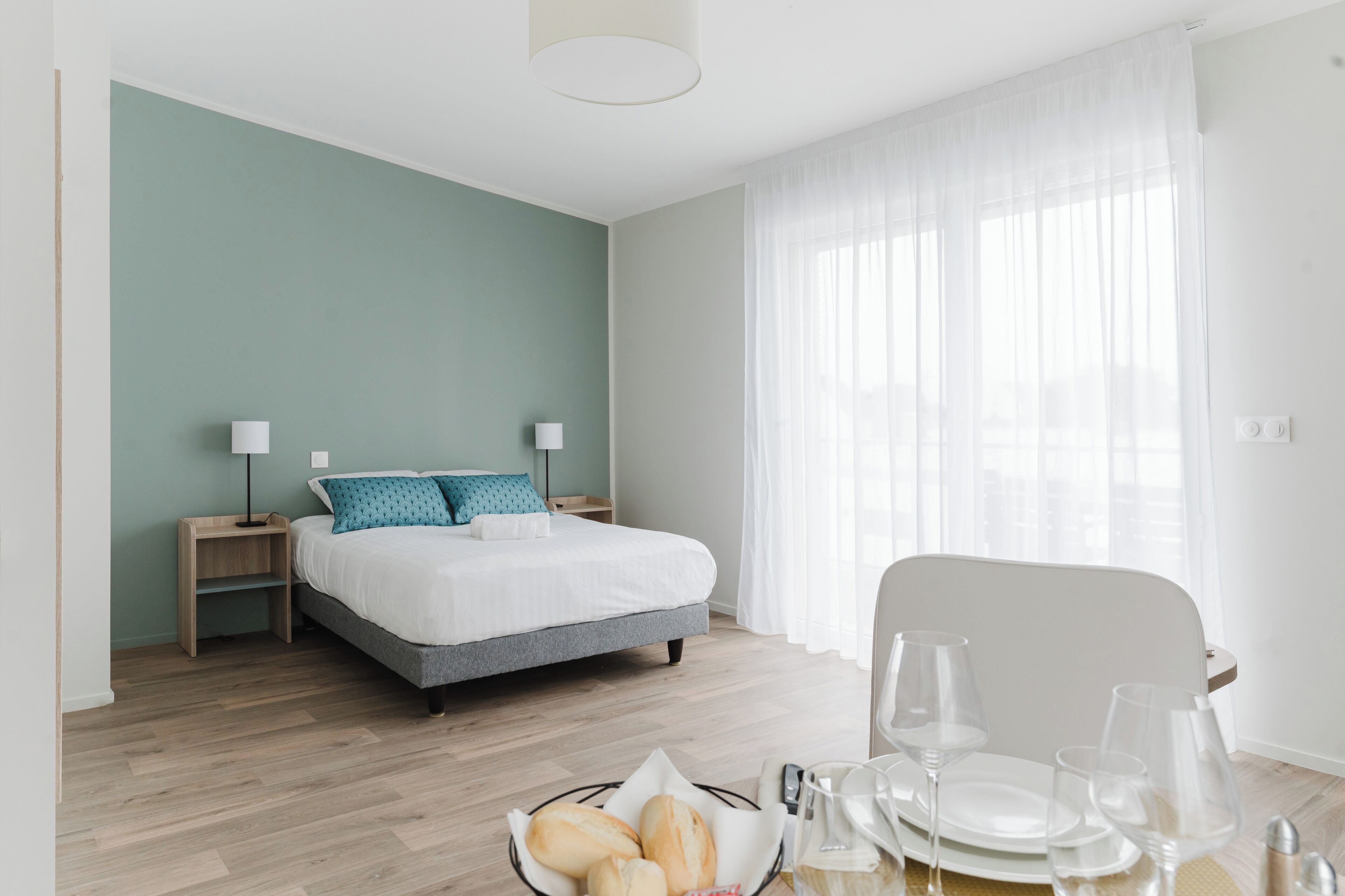 A bedroom with a bed, bedside tables, a dining table with chairs, and a window with curtains.