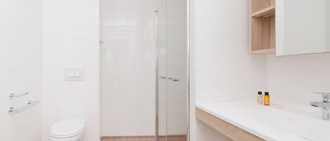 Un baño moderno con inodoro, cabina de ducha de vidrio y lavamanos blanco con encimera de madera.
