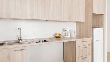 Una cocina moderna con armarios de madera clara, un lavamanos de acero inoxidable, una cafetera y un refrigerador blanco.