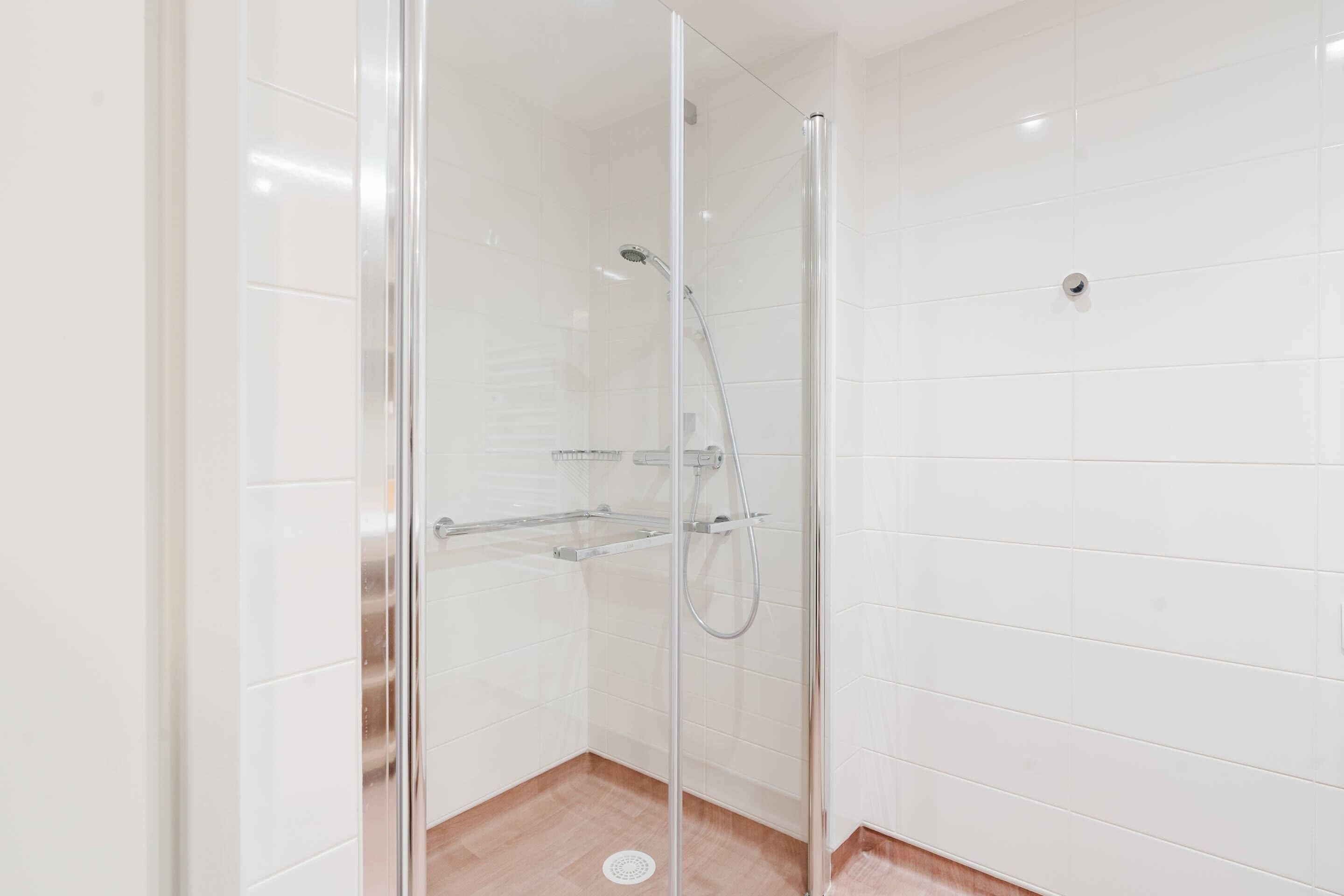 Ducha con cerramiento de vidrio, cabezal de ducha manual y llave en la pared.