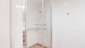 Ducha con cerramiento de vidrio, cabezal de ducha manual y llave en la pared.