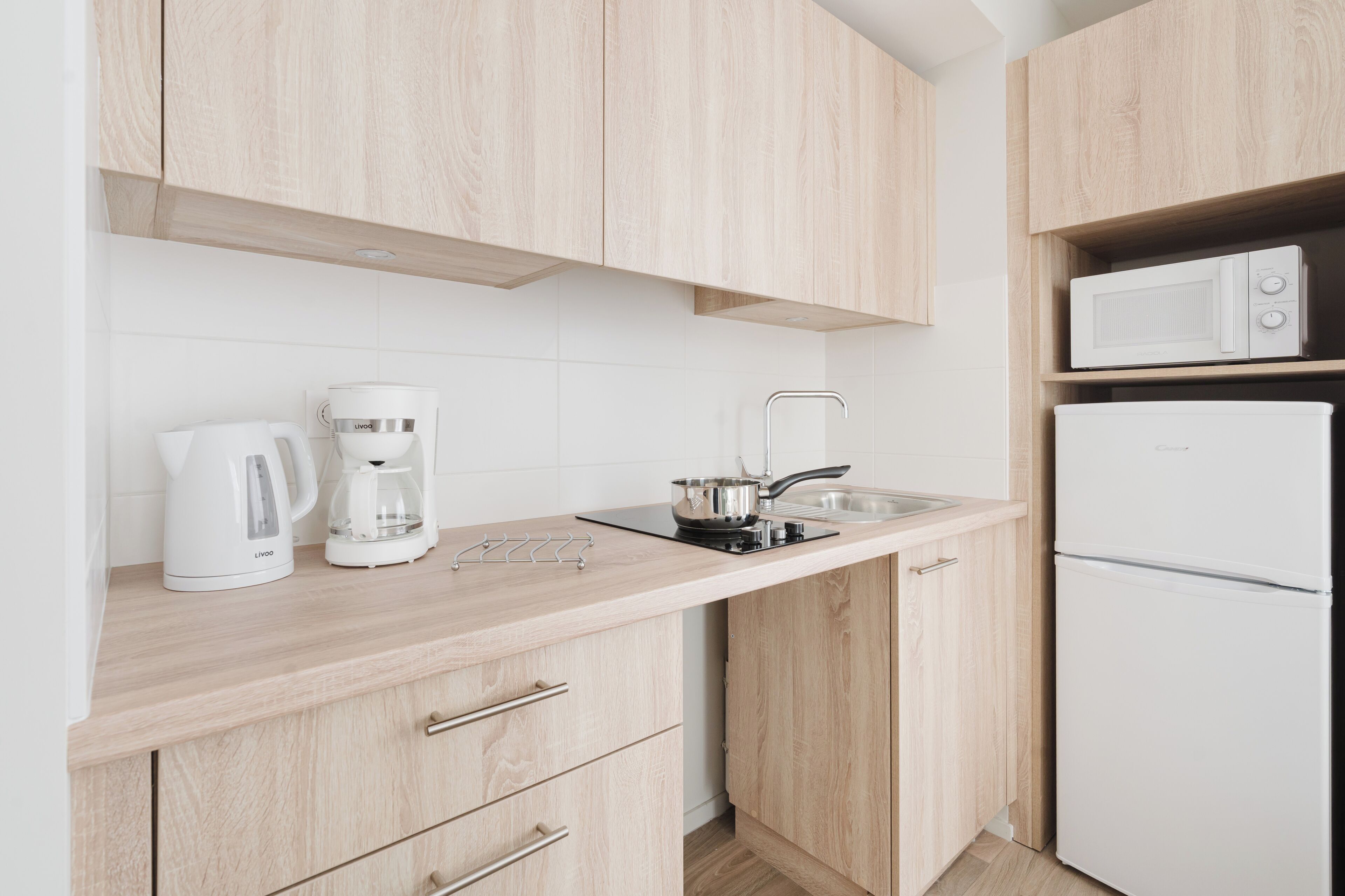Una cocina moderna con armarios de madera clara, un refrigerador blanco, un microondas, una cafetera y un hervidor.