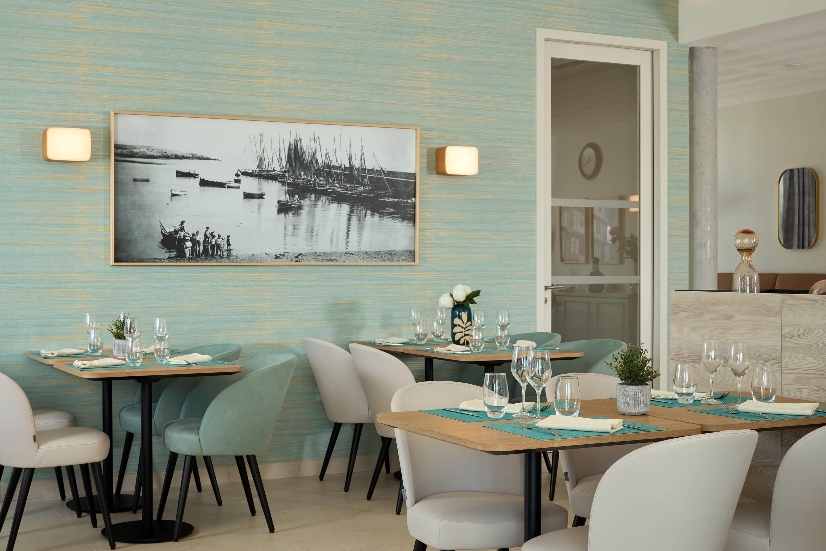 A dining area with tables set for two, chairs, and a wall-mounted picture.