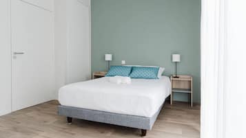 A neatly made bed with white bedding and teal pillows, two bedside tables with lamps, and a light green wall.