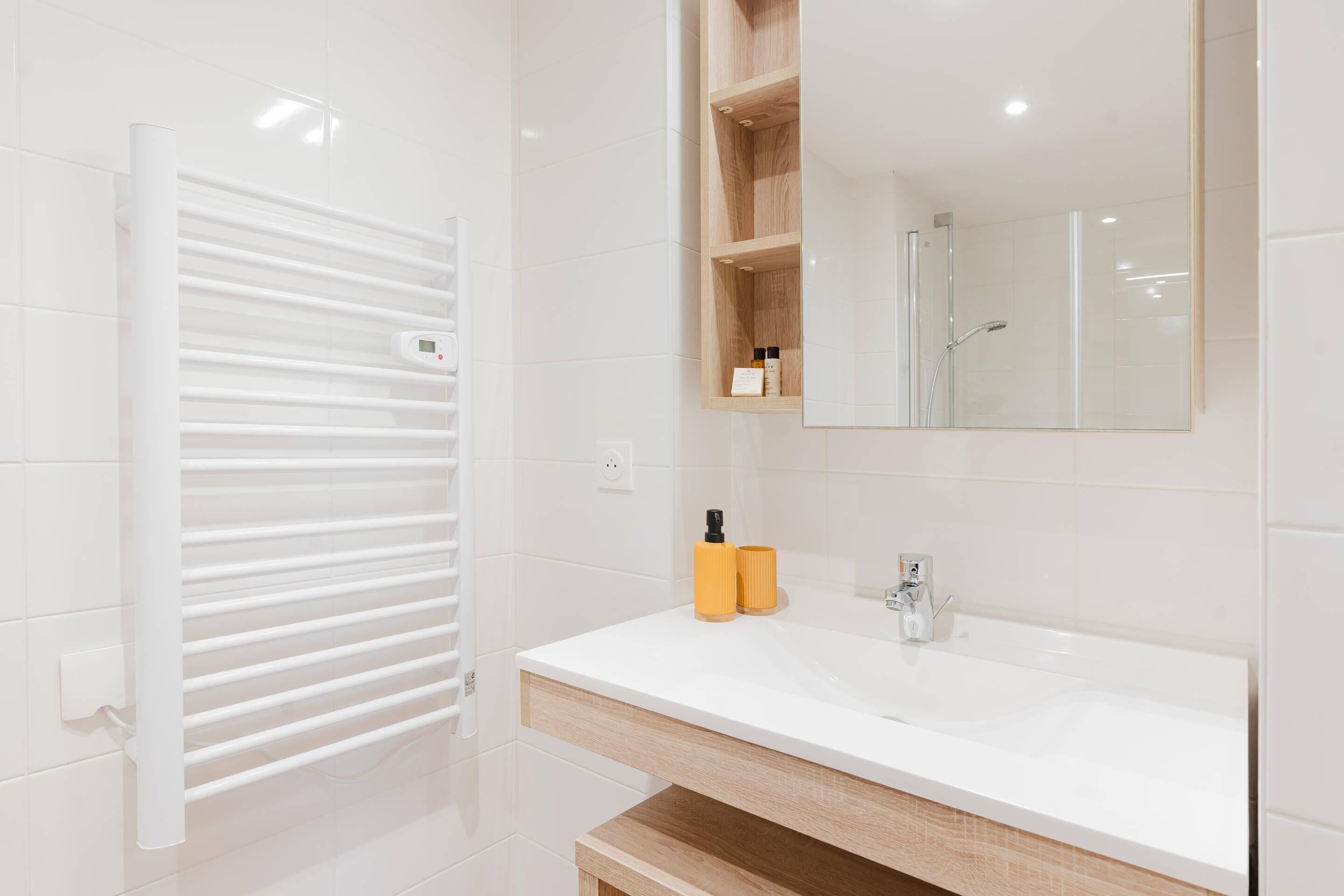 A modern bathroom with a white vanity, a mirror, a towel rack, and a shower area.