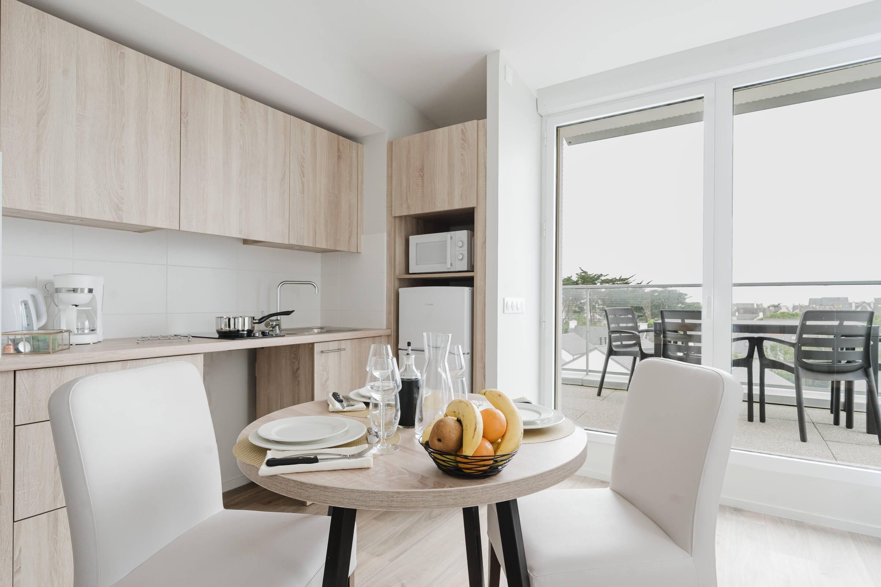 Eine moderne Küche mit Holzausstattung, ein Essbereich mit rundem Tisch und Blick auf die Stadt durch große Fenster.