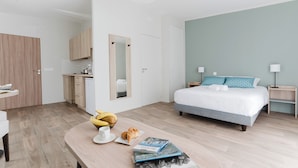 Une chambre d’hôtel moderne équipée d’un lit, de tables de chevet, d’un bureau et d’une kitchenette.