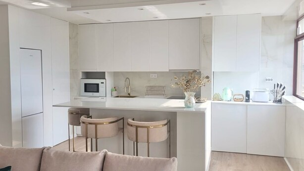 A modern kitchen with white cabinetry, a built-in microwave, and a bar area with stools. - Apartment Apulia - sea view 6 people (Apúlia esposende)