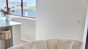 A modern living room with a curved sectional sofa, a small side table, and a view of the sea through large windows. - Apartment Apulia - sea view 6 people (Apúlia esposende)
