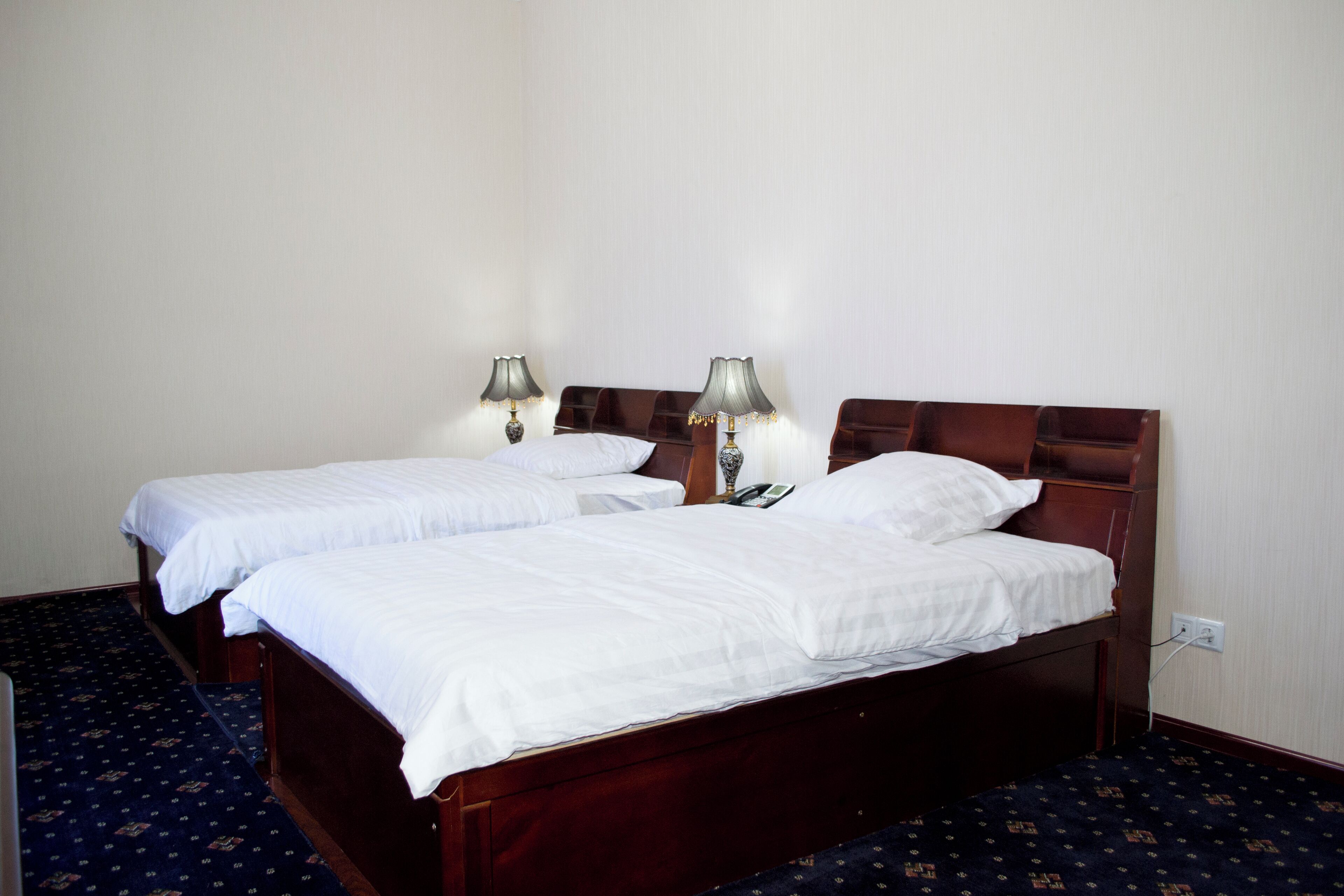 A hotel room with two single beds, each with a wooden headboard, white linens, and two bedside lamps.