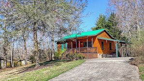 A log cabin with a green roof, a porch, and a driveway leading to the entrance. - Cozy Cove Retreat by Chatuge Home Concierge | Private Swim Dock, Kayaks & Grill (Hayesville)