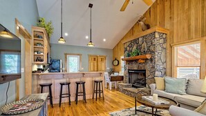 A spacious living area with a stone fireplace, wooden accents, a kitchen with a bar, and a cozy seating area. - Cozy Cove Retreat by Chatuge Home Concierge | Private Swim Dock, Kayaks & Grill (Hayesville)