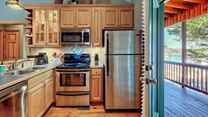 A modern kitchen with stainless steel appliances, wooden cabinets, and a view of the outdoors through a sliding glass door. - Cozy Cove Retreat by Chatuge Home Concierge | Private Swim Dock, Kayaks & Grill (Hayesville)