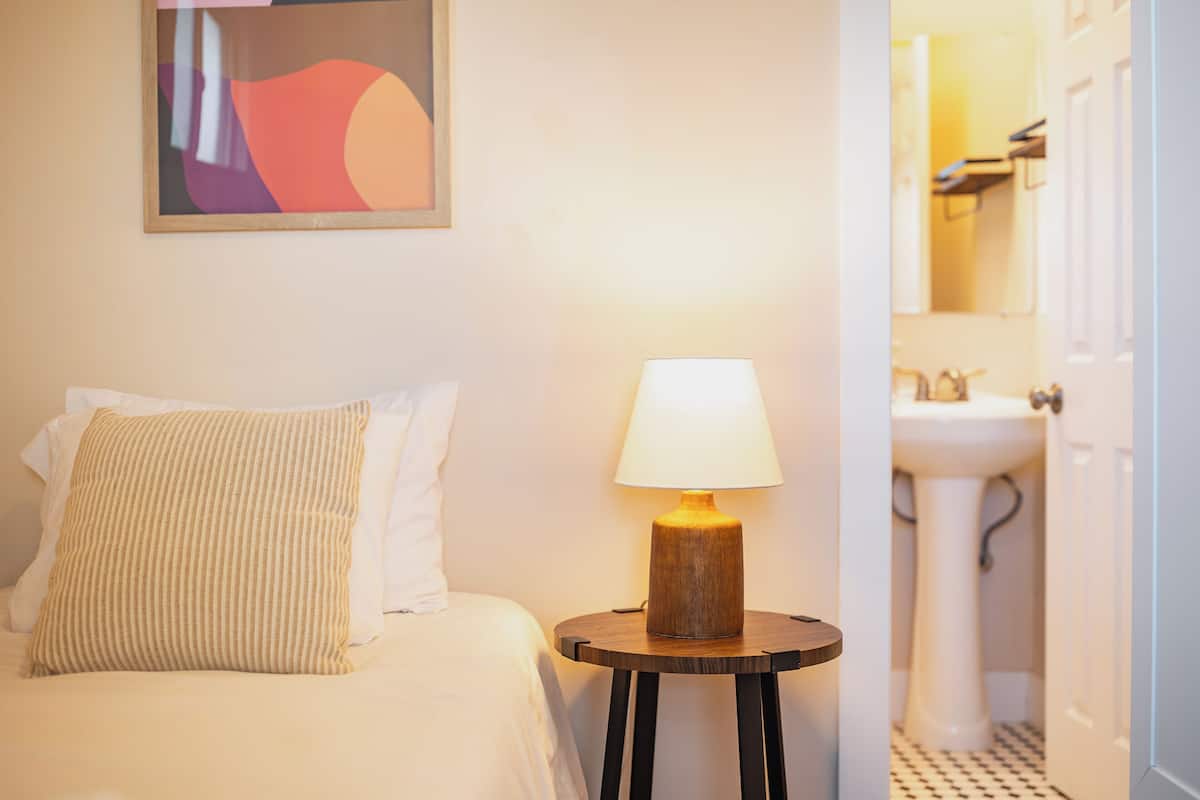 Een hotelkamer met een bed, een bedlamp, een schilderij aan de muur, en een badkamer die door een open deur zichtbaar is.