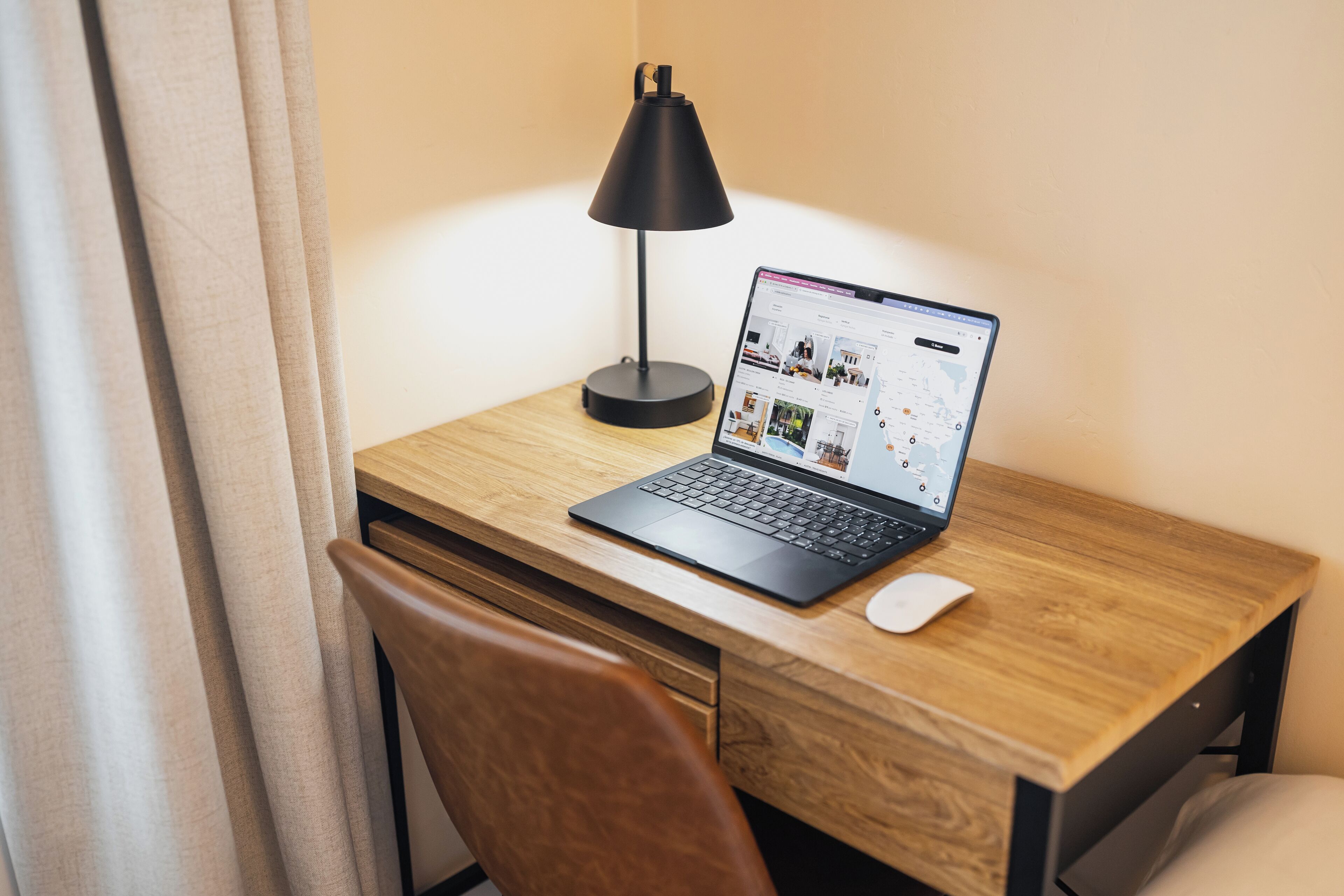 En bærbar computer på et træbord med en sort lampe, en hvid mus og en træstol.