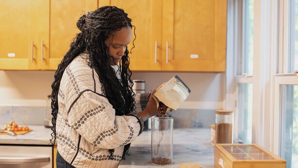 A person pouring coffee beans into a glass jar in a kitchen with wooden cabinets and a window. - Outsite San Diego - Golden Hill - Work, Connect, Explore (San Diego)