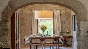 Un coin repas avec un mur en pierre, une table en bois dressée pour quatre personnes et une fenêtre agrémentée de rideaux.