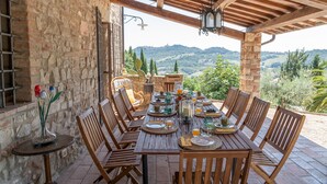An outdoor dining area with a stone wall, wooden chairs, and a table set for a meal. - Villa la Pizzichina 10 Emma Villas (Todi)