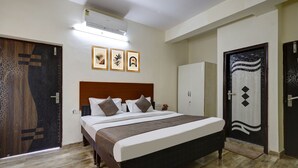 A bedroom with a wooden headboard, a bed with white bedding, a bedside table, and a wardrobe. There are three framed pictures on the wall, an air conditioning unit, and a door with a decorative pattern. - Hotel Spectrum Inn - By ASPL (Noida)