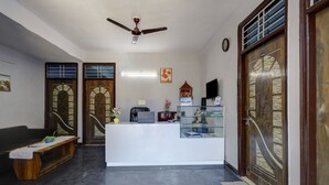 A reception area with a reception desk, a bench, a ceiling fan, and a wall-mounted clock. - Hotel Spectrum Inn - By ASPL (Noida)