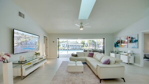 Un salon spacieux avec un canapé blanc, une table basse et un téléviseur à écran plat qui affiche « CoralVilla Villa & Boat Rental ».