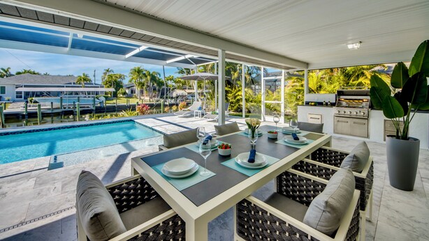 Un espace repas aménagé au bord de la piscine, avec une table pour deux, un barbecue et une vue sur la piscine et les environs.