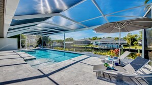 Un espace piscine extérieur moderne offrant une vue dégagée sur le paysage environnant, notamment sur une maison et des palmiers.