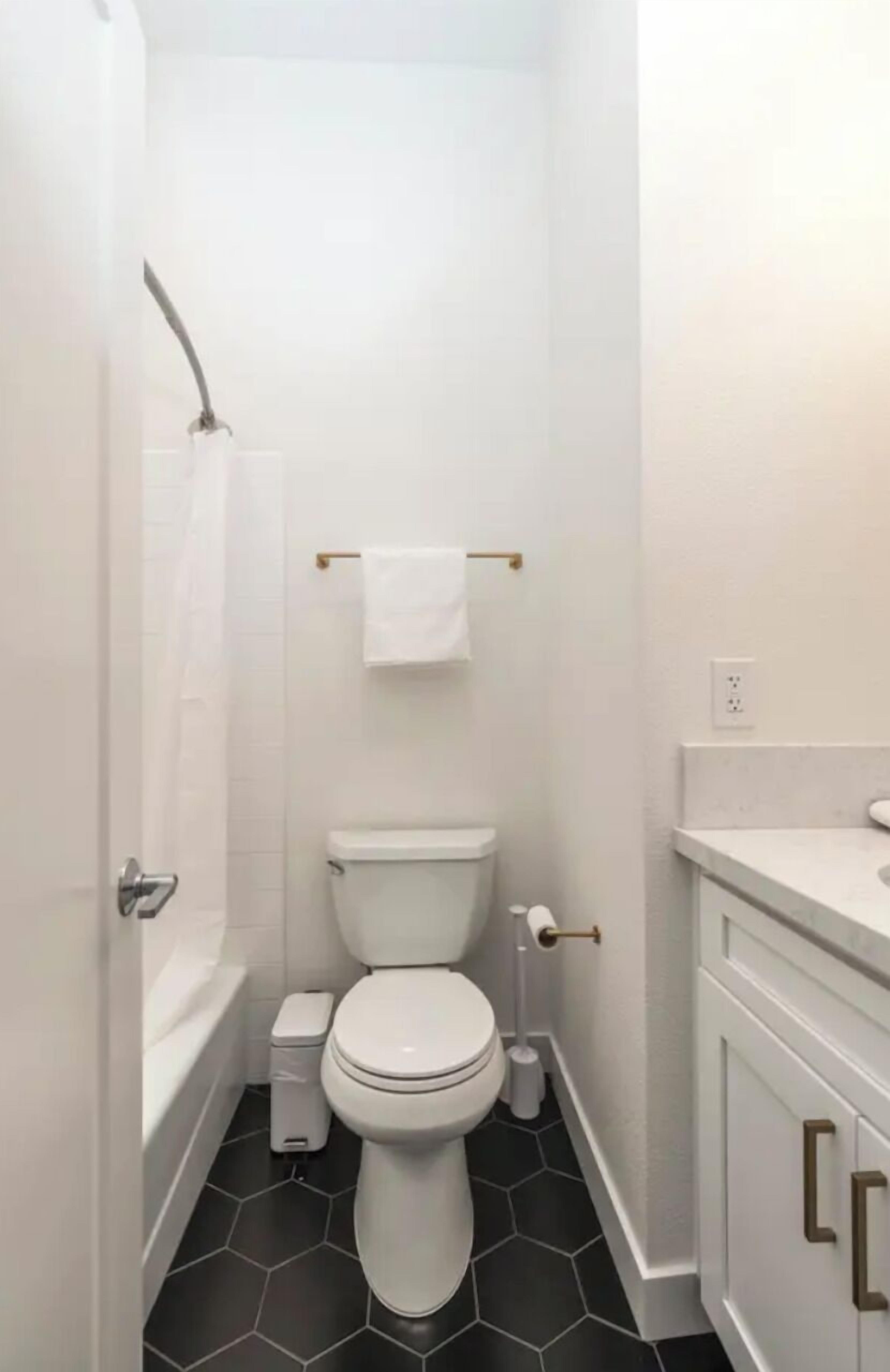 Une petite salle de bain compacte, avec des toilettes blanches, un lavabo blanc et une baignoire.