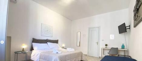 A hotel room with a bed, bedside table, desk, chair, and a TV mounted on the wall.