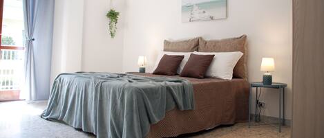 A bedroom with a bed, two bedside tables with lamps, a hanging plant, and a painting on the wall.