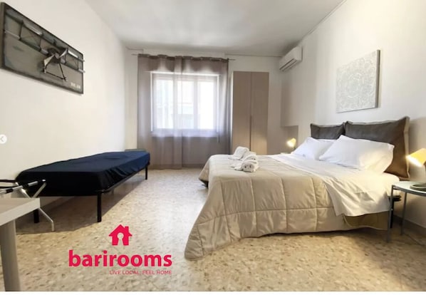 A hotel room with a bed, bedside table, and a window with curtains.