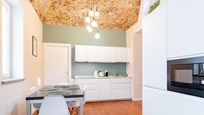 Une cuisine moderne avec des meubles blancs, une table à manger en bois et des chaises, ainsi qu’un plafond au revêtement original.