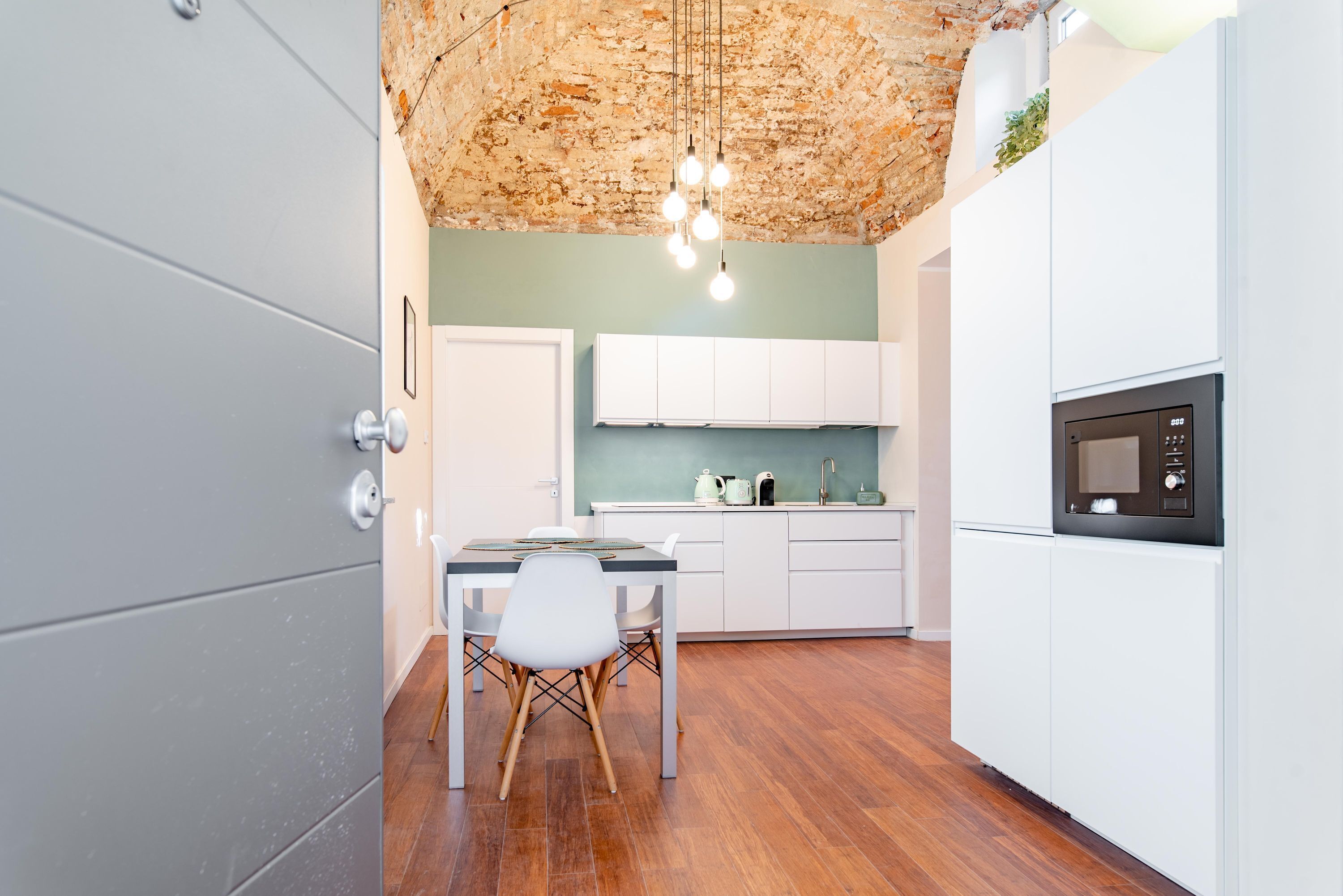 A modern kitchen with white cabinets, a wooden dining table, and a hanging light fixture.
